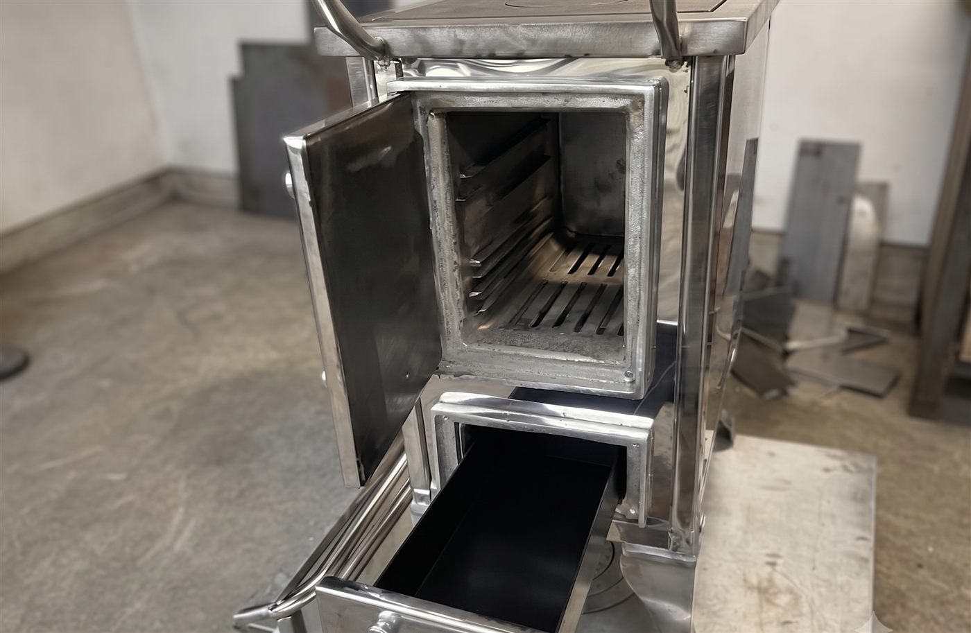 Cocina a leña de acero inoxidable con el horno abierto, mostrando las parrillas interiores