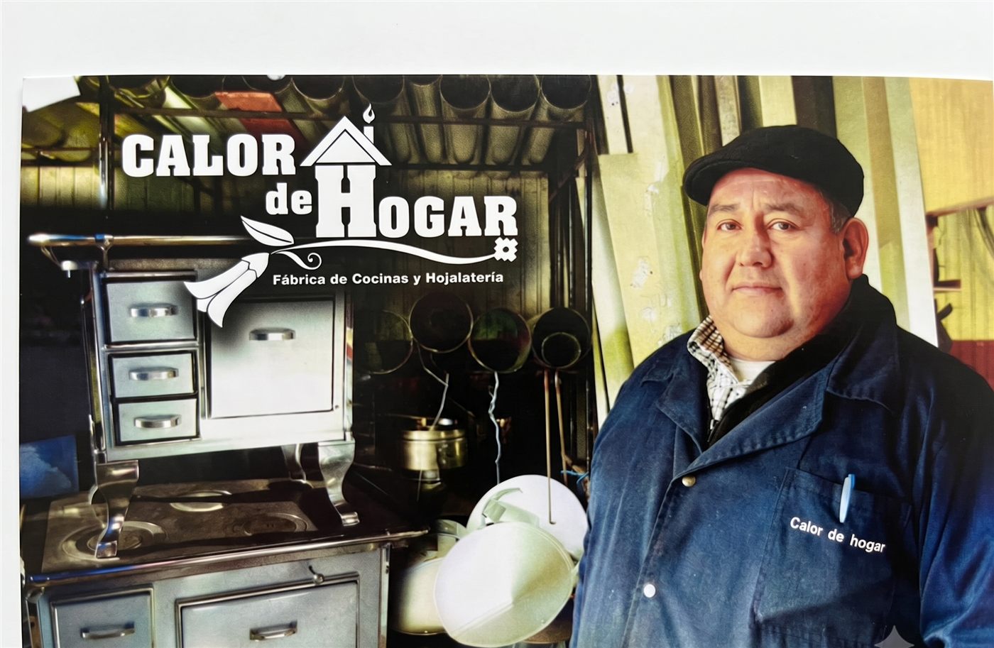 Miguel A. Bustamante con su overol de trabajo, junto a una cocina a leña terminada y el logo de Calor de Hogar