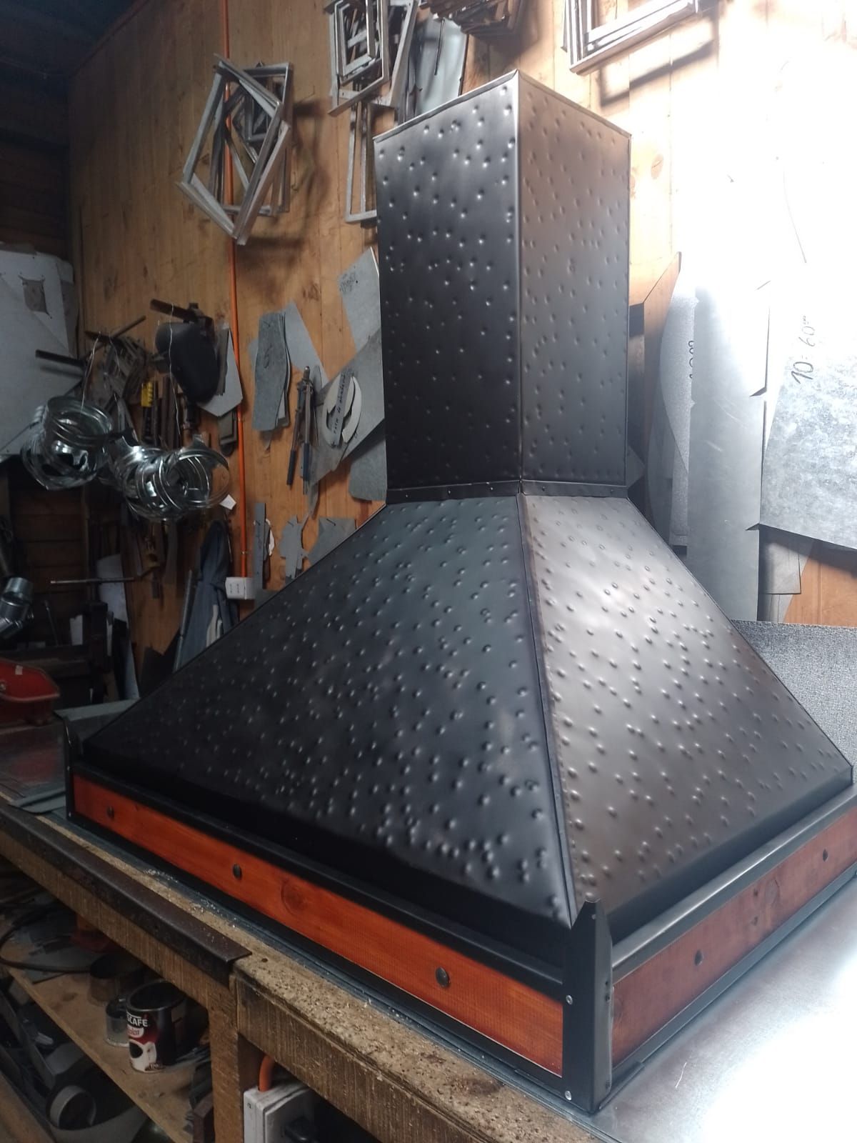 Campana negra de plancha martillada a mano con banda de madera barnizada, terminada sobre el mesón del taller